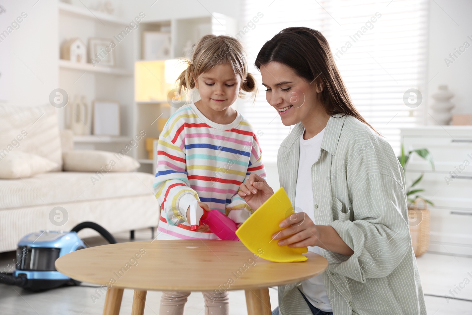 Photo of Cute little girl helping her mother wiping wooden table at home