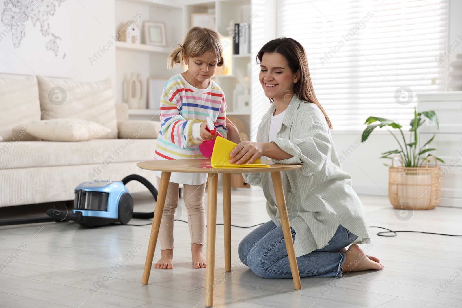 Photo of Cute little girl helping her mother wiping wooden table at home