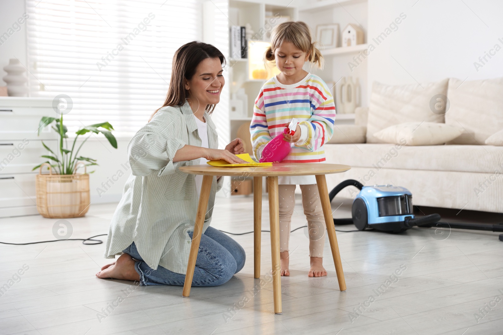 Photo of Cute little girl helping her mother wiping wooden table at home