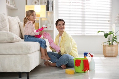 Photo of Little helper. Cute girl giving her mother spray bottle of cleaning product at home