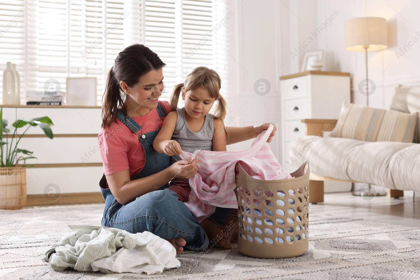 Photo of Little girl helping her mother taking out laundry from basket at home