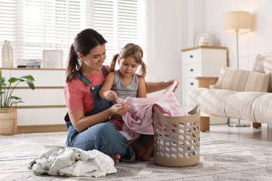 Little girl helping her mother taking out laundry from basket at home