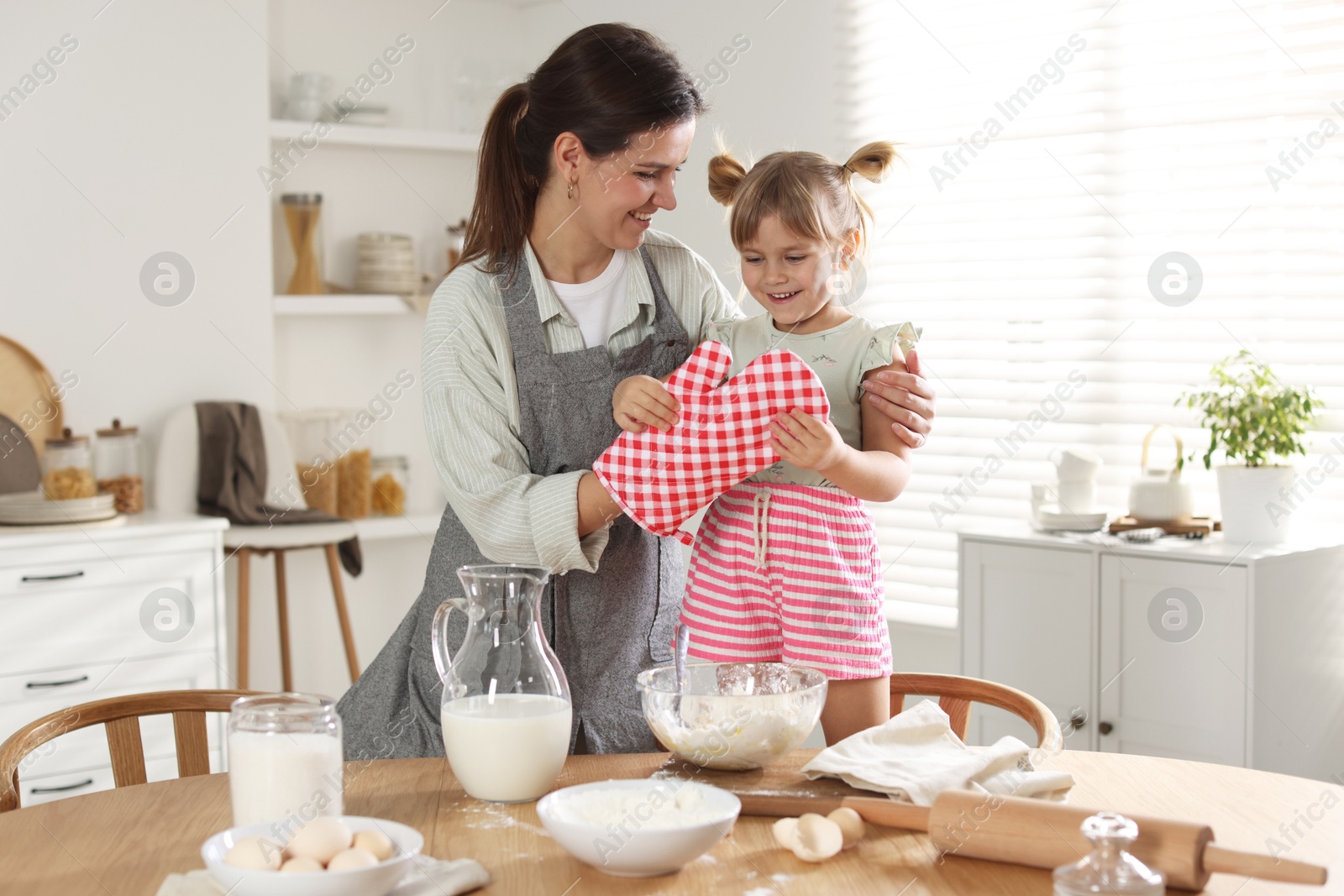 Photo of Mother with her little daughter cooking together at table in kitchen