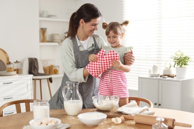 Photo of Mother with her little daughter cooking together at table in kitchen