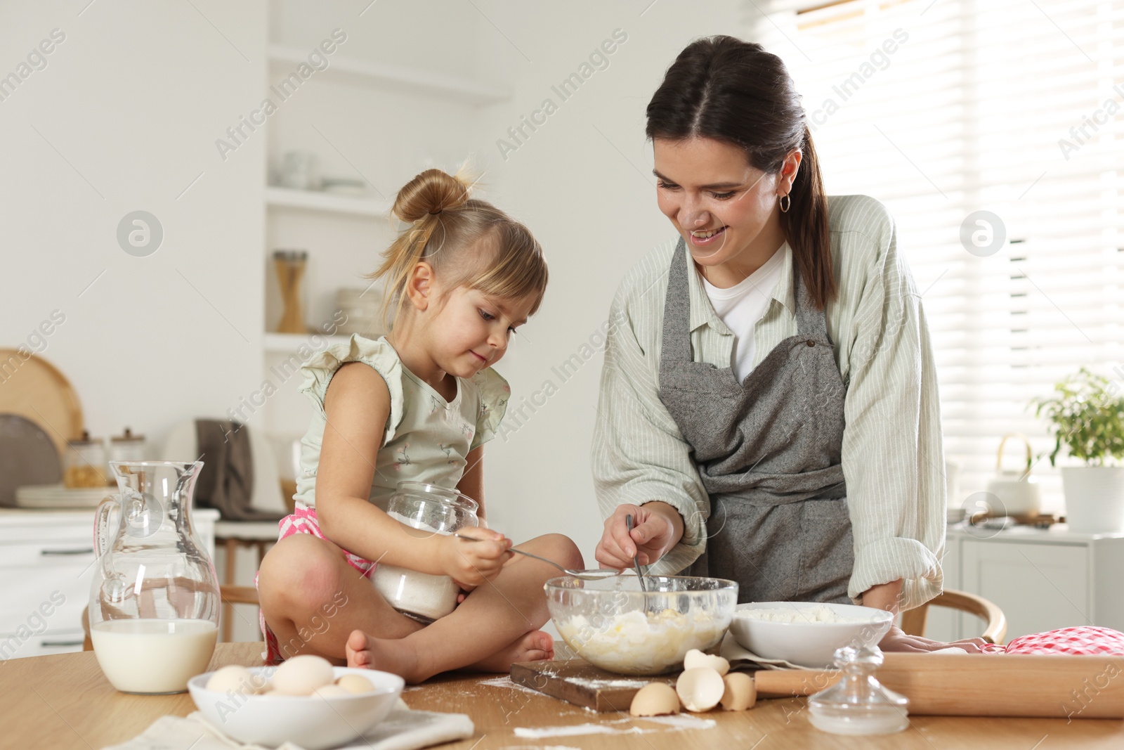 Photo of Little girl helping her mom making dough at table in kitchen