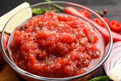 Photo of Spicy salsa sauce in bowl and ingredients on table, closeup