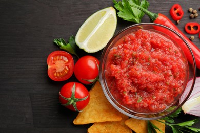 Spicy salsa sauce in bowl, nachos and ingredients on wooden table, flat lay. Space for text