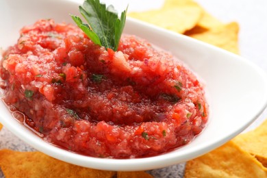 Spicy salsa sauce in gravy boat and nachos on table, closeup