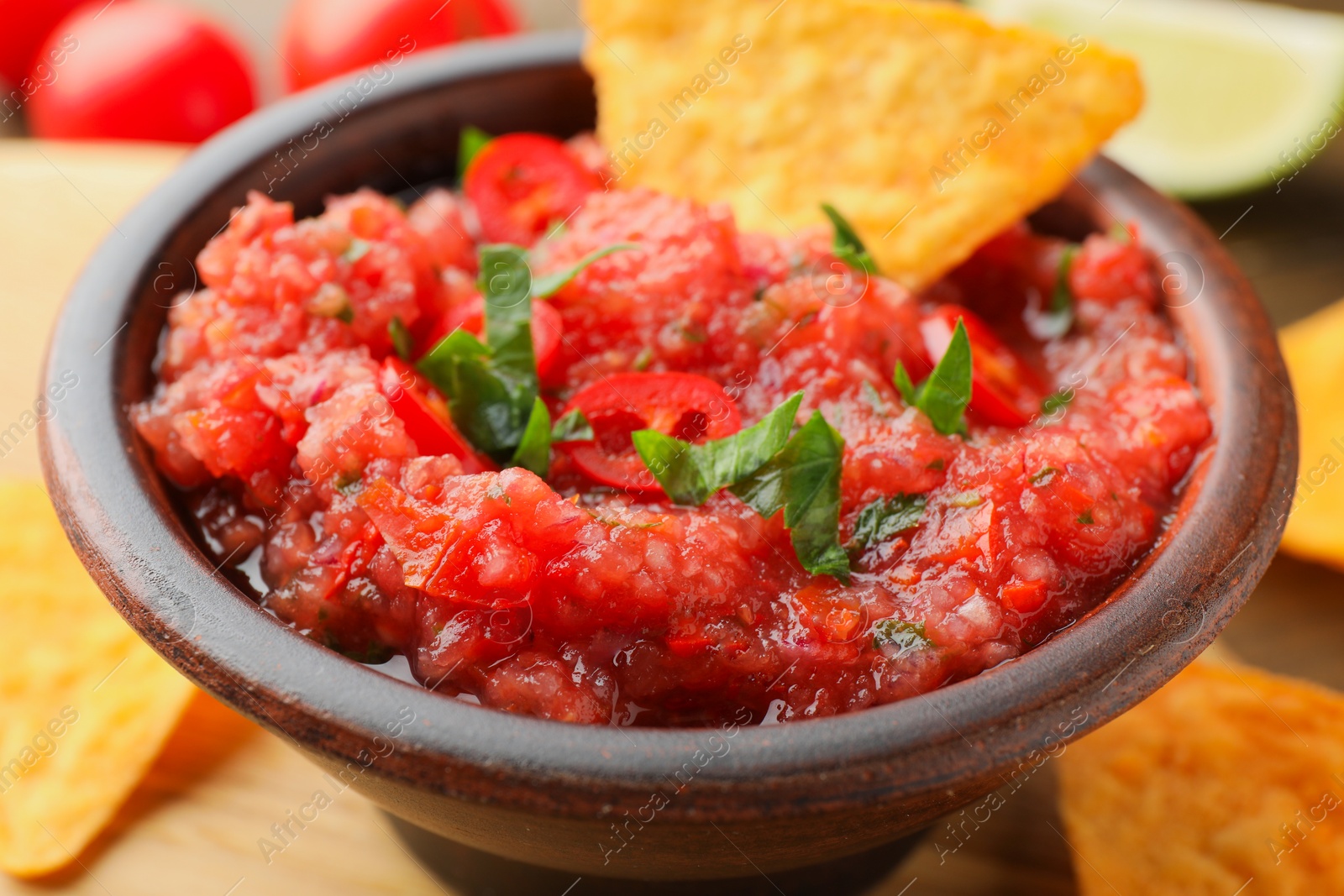 Photo of Spicy salsa sauce in bowl and nachos on table, closeup