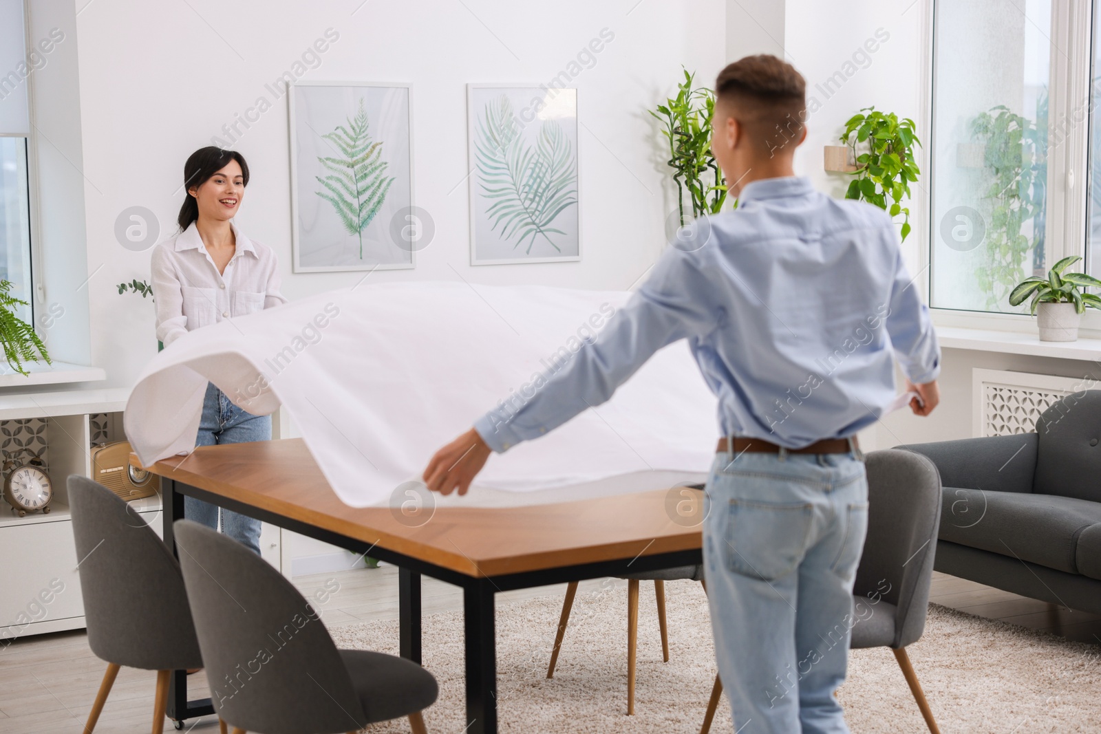 Photo of Couple putting white tablecloth on table at home