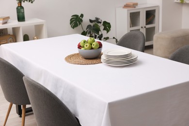 Table with white tablecloth, apples, plates and chairs in stylish room