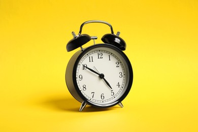 Photo of One black alarm clock on yellow background