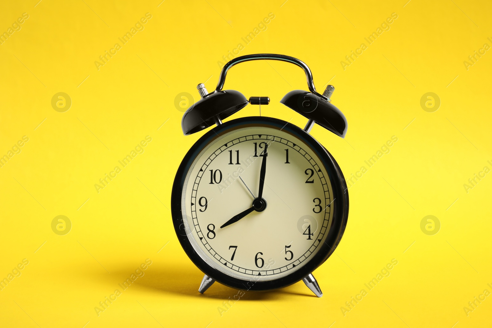Photo of One black alarm clock on yellow background
