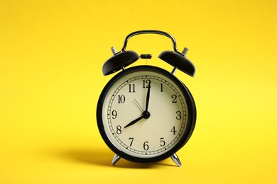 Photo of One black alarm clock on yellow background