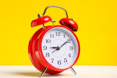 Photo of One red alarm clock on white wooden table against yellow background
