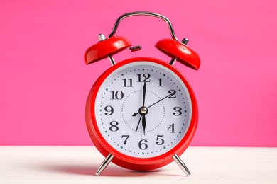 Photo of One red alarm clock on white wooden table against bright pink background