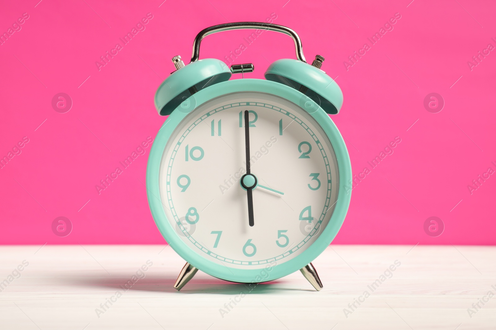 Photo of One turquoise alarm clock on white wooden table against bright pink background