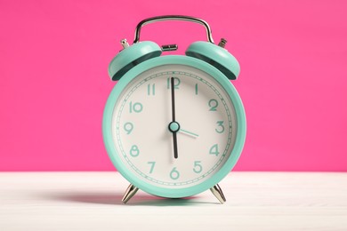 Photo of One turquoise alarm clock on white wooden table against bright pink background