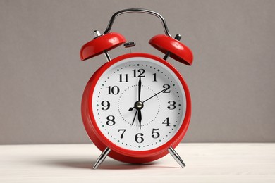 Photo of One red alarm clock on white wooden table against grey background
