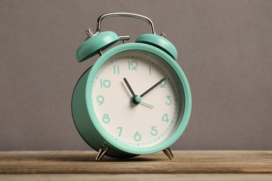 Photo of One turquoise alarm clock on wooden table against grey background