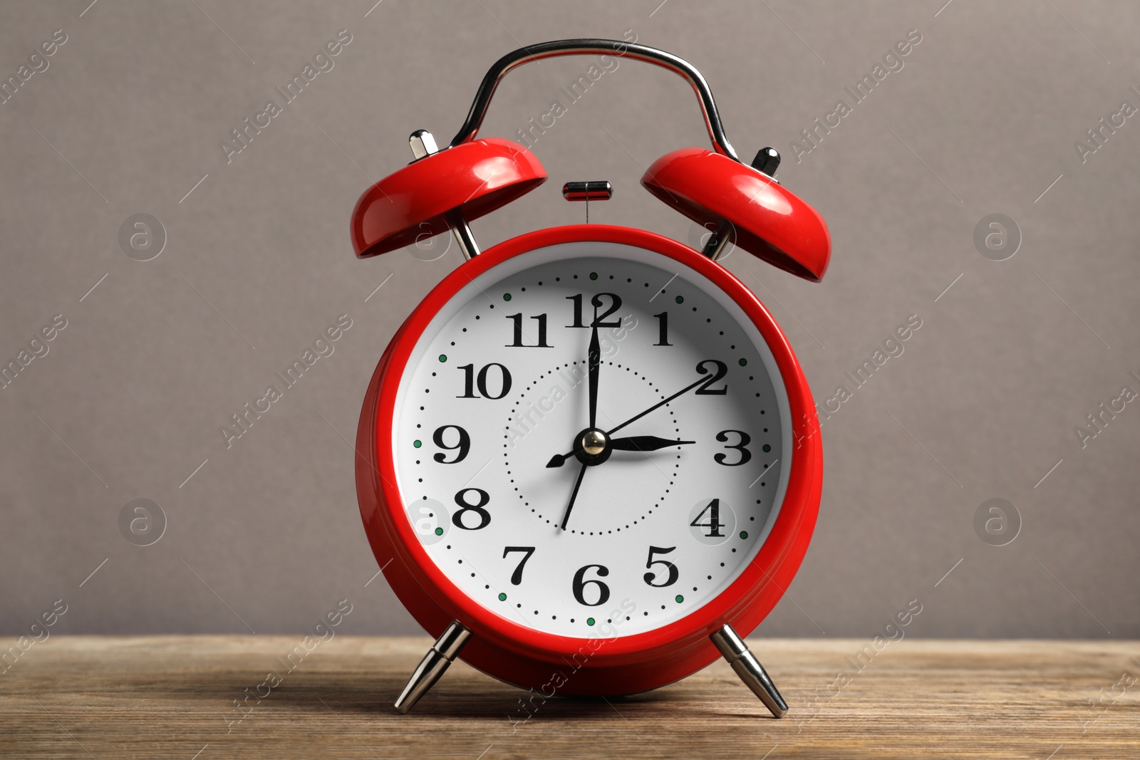 One red alarm clock on wooden table against grey background Photo of One red alarm clock on wooden table against grey background