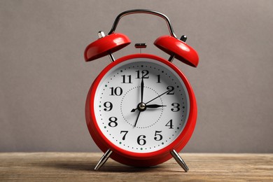 Photo of One red alarm clock on wooden table against grey background