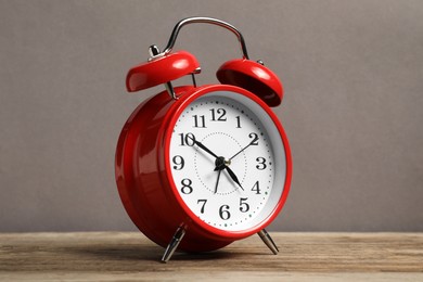 Photo of One red alarm clock on wooden table against grey background