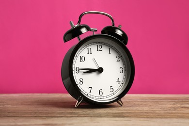Photo of One black alarm clock on wooden table against bright pink background