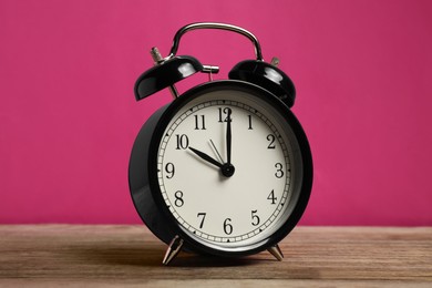 Photo of One black alarm clock on wooden table against bright pink background