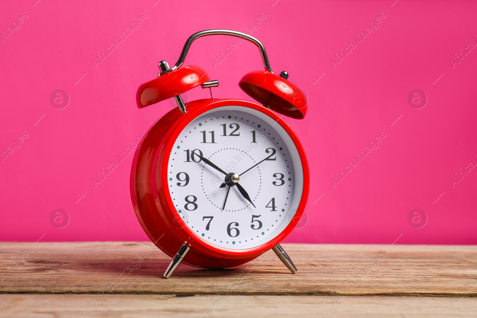 One red alarm clock on wooden table against bright pink background Photo of One red alarm clock on wooden table against bright pink background