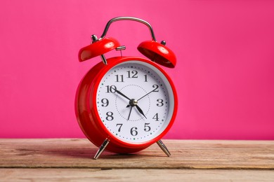 Photo of One red alarm clock on wooden table against bright pink background