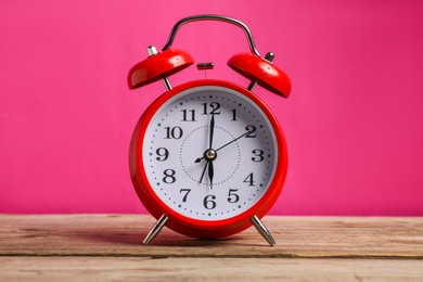 Photo of One red alarm clock on wooden table against bright pink background