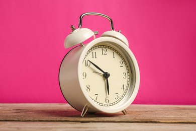 Photo of One white alarm clock on wooden table against bright pink background