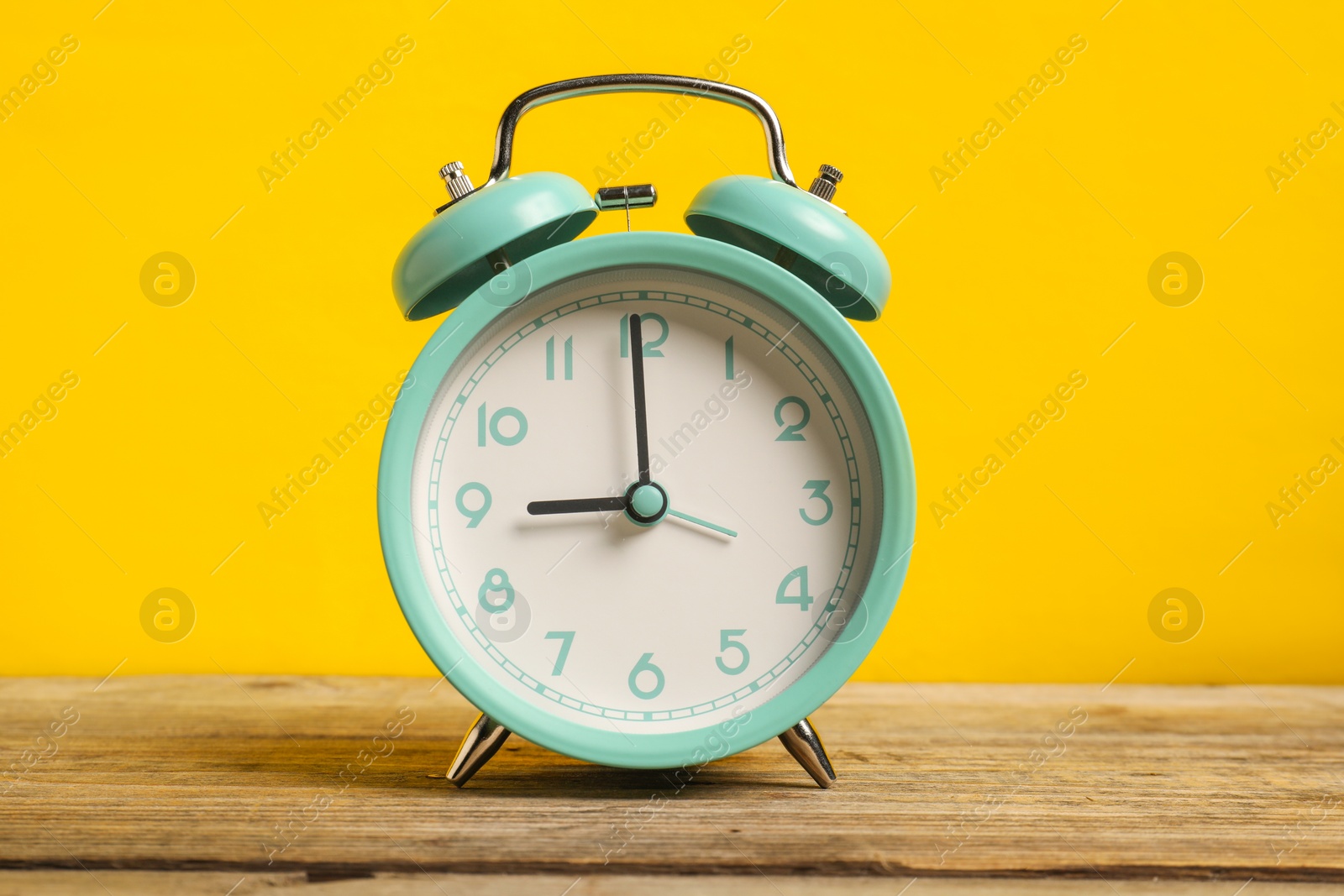 Photo of One turquoise alarm clock on wooden table against yellow background