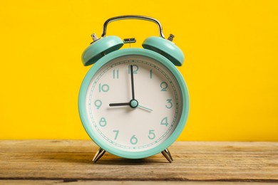 Photo of One turquoise alarm clock on wooden table against yellow background
