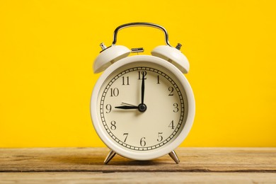 Photo of One white alarm clock on wooden table against yellow background
