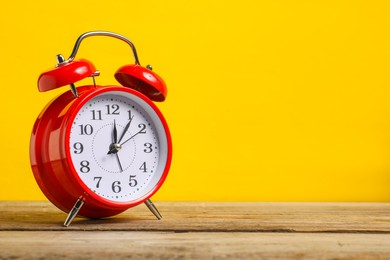 Photo of One red alarm clock on wooden table against yellow background, space for text