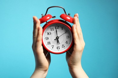 Photo of Woman with red alarm clock on light blue background, closeup