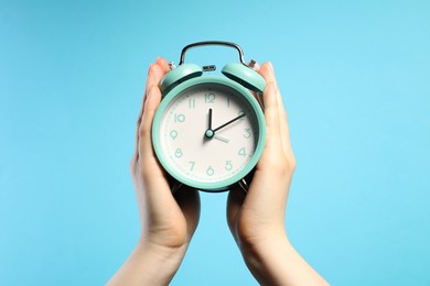 Photo of Woman with turquoise alarm clock on light blue background, closeup