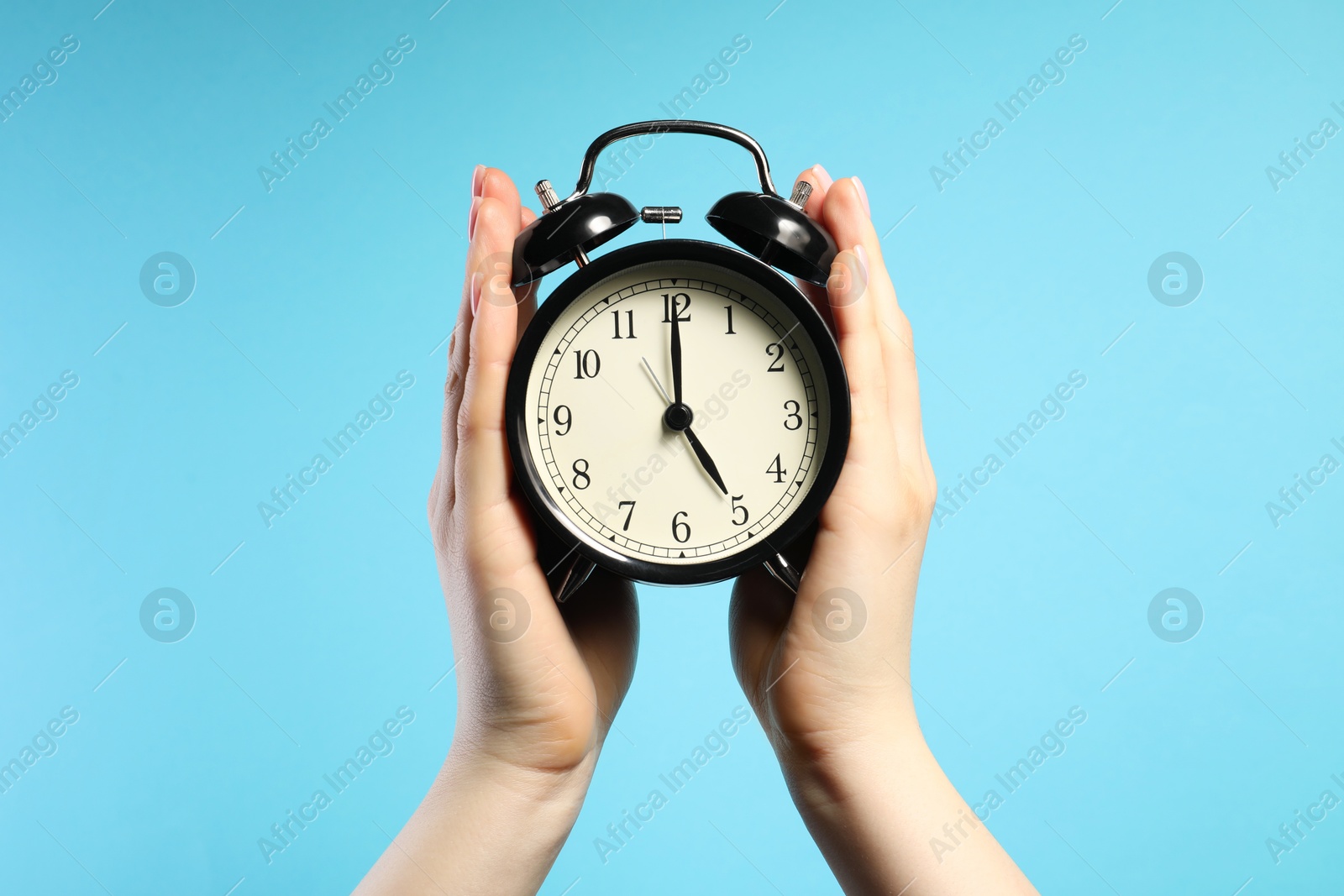 Photo of Woman with black alarm clock on light blue background, closeup