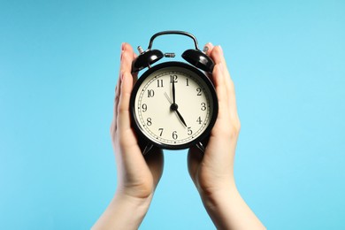 Photo of Woman with black alarm clock on light blue background, closeup