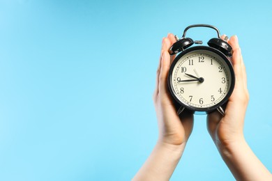Photo of Woman with black alarm clock on light blue background, closeup. Space for text