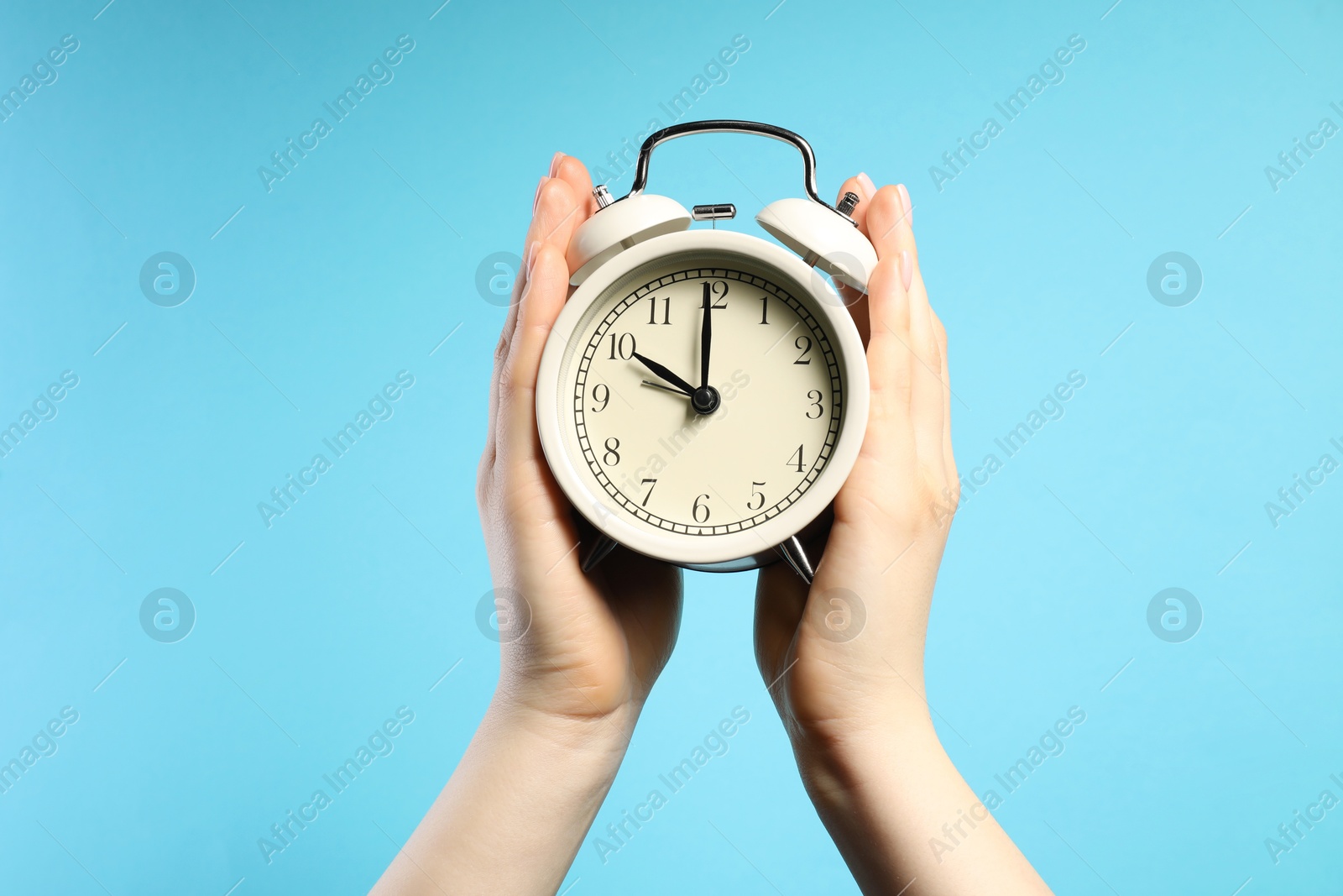 Woman with white alarm clock on light blue background, closeup Photo of Woman with white alarm clock on light blue background, closeup