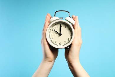 Photo of Woman with white alarm clock on light blue background, closeup