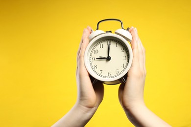 Photo of Woman with white alarm clock on yellow background, closeup. Space for text