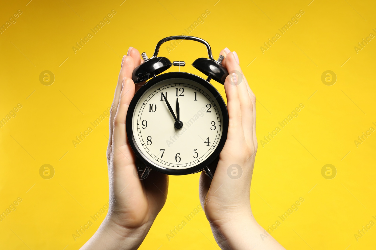 Woman with black alarm clock on yellow background, closeup Photo of Woman with black alarm clock on yellow background, closeup