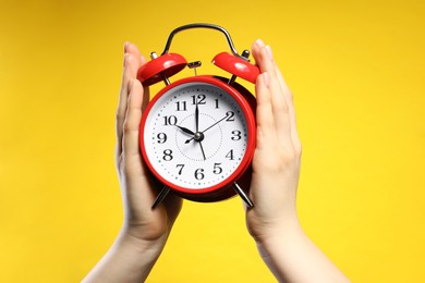 Photo of Woman with red alarm clock on yellow background, closeup