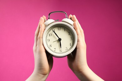 Photo of Woman with white alarm clock on bright pink background, closeup
