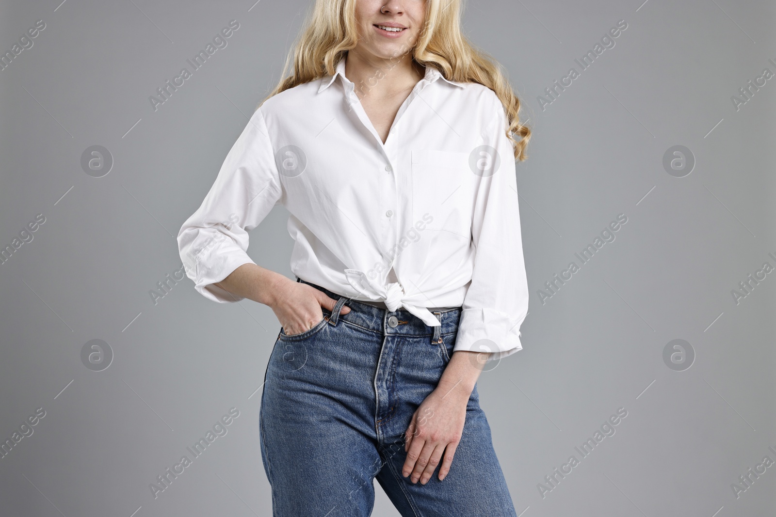 Photo of Smiling woman in stylish jeans on grey background, closeup