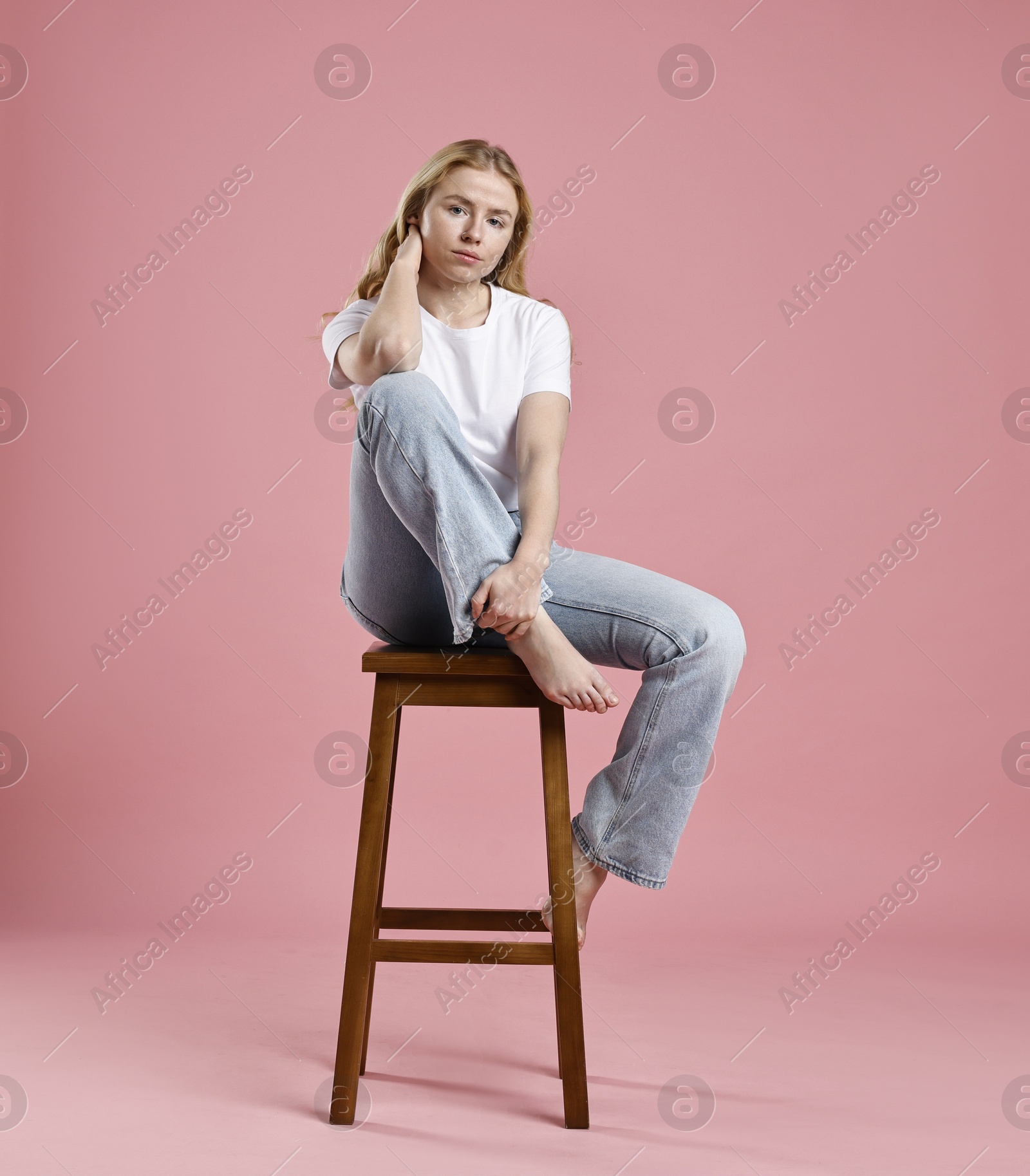 Photo of Beautiful young woman in stylish jeans sitting on stool against pink background